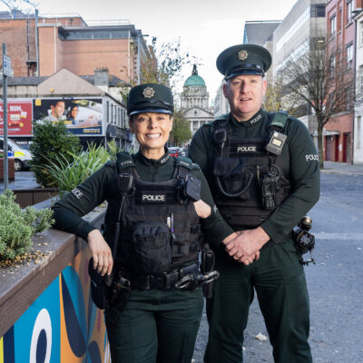 A smiling woman police officer stands next to a smiling male police officer. They stand next to a parklet that was built by LQ BID.