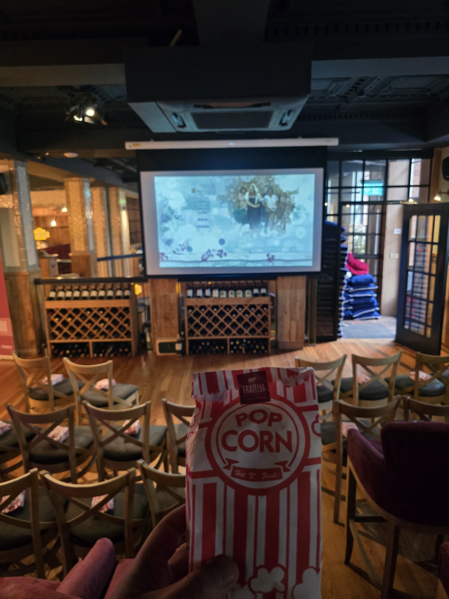 image shows red and white striped pp corn bag held in front of a screen and chairs each hosting a bag of popcorn