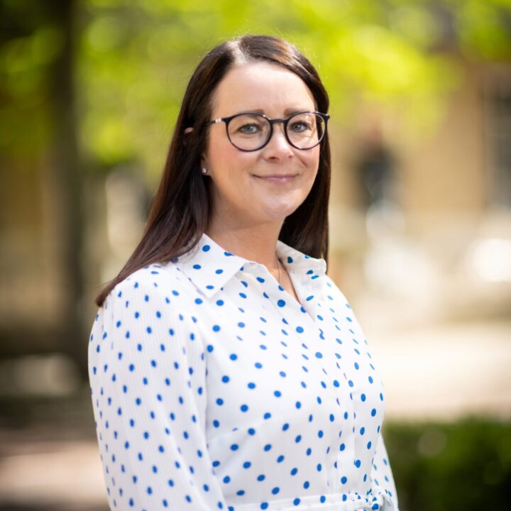 Jeanette Donohoe in a white blouse with black spots, wearing her hair down and glasses