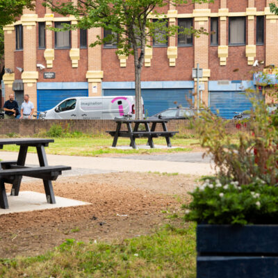 Two black benches in a park with a white van in the background