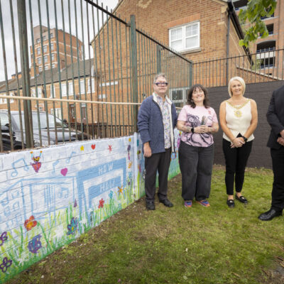 Lord Mayor and three others stand in front of colourful childrens mural which depicts harland and wolff cranes
