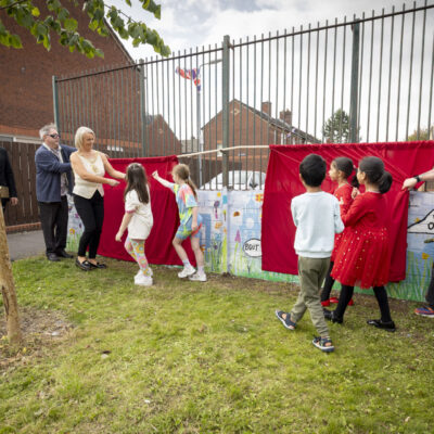 Children and Lord Mayor and another man hold a red banner shielding their mural from sight before it is unveiled