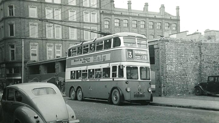 AEC 62 is at the Castle Street where the Falls Road and Glen Road buses departed. The bomb-damaged buildings in the background dates the picture to the early 1950s. The trolley poles are on the left-hand pair of wires which means that she is on a cross-town service from Whitehouse or Whitewell. The bus is well packed, mainly with women.