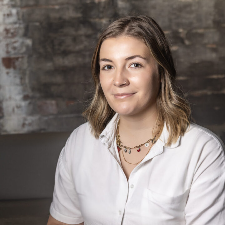 A-woman poses in front of a brick background wearing a white shirt
